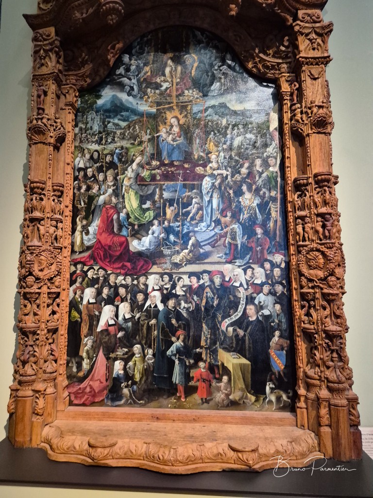 Tableau complexe représentant une scène religieuse avec la Vierge Marie et de nombreux personnages dans un cadre en bois sculpté.